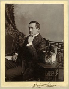 Un jeune homme moustachu, portant un veston, est assis et pose pour un portrait formel, la main gauche sous le menton.