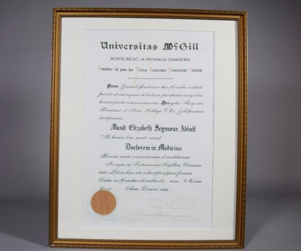 Diplôme de l’Université McGill. « Doctorem in Medicina » décerné à « Maud Elizabeth Seymour Abbott » par l’Université McGill. Le texte sur le diplôme est en latin. Dans le coin inférieur gauche, le sceau rouge de l’Université McGill, à sa droite, de nombreuses signatures. Le diplôme est dans un mince cadre doré et simplement orné et un passepartout blanc.