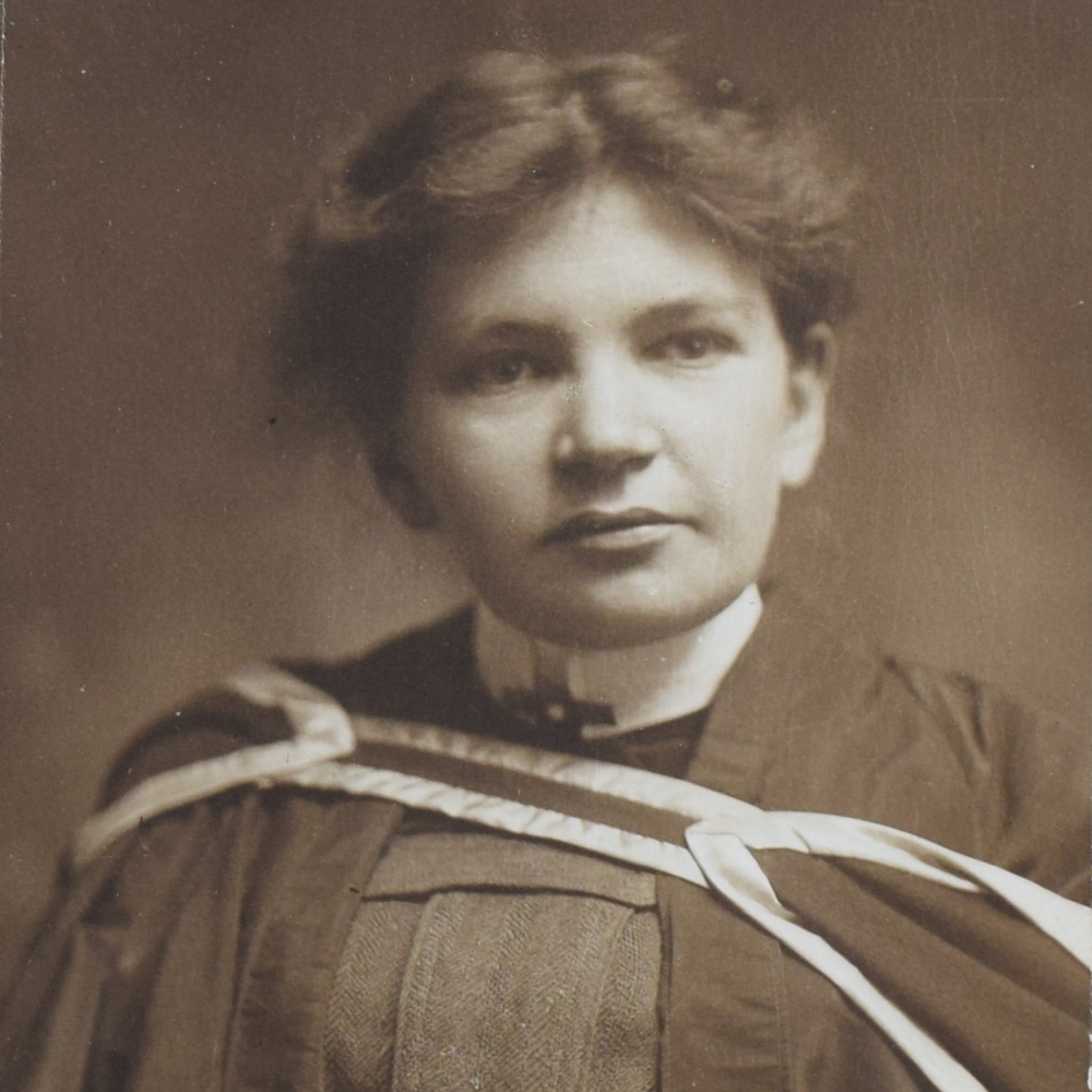 Photographie en noir et blanc de Maude Abbott, jeune adulte, tête et épaules. Elle porte un habit et une toge de graduation. Ses cheveux foncés sont attachés à l’arrière de sa tête et sa tête est légèrement tournée vers la gauche.