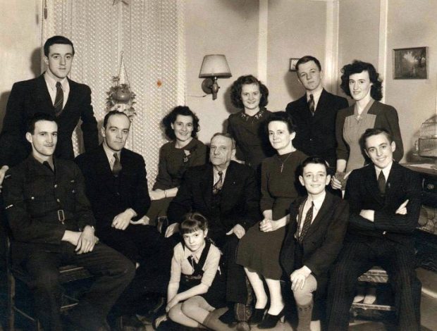 Photographie en noir et blanc d’Hélène B.-Beauséjour, son conjoint et ses dix enfants. Hélène B.-Beauséjour et son conjoint sont au centre de la photographie. À leur gauche, un fils est assis. À leur droite, trois des fils posent pour une photographie. Derrière eux se trouvent trois de leurs filles et un de leurs fils. Devant eux, deux enfants, un garçon et une fille, sont assis au sol. 