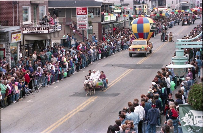 Photograph of a parade organized as part of the Louiseville Buckwheat Pancake Festival. A float pulled by a pony is making its way down the town’s main thoroughfare. People are looking on from either side of the street.