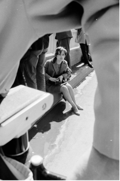 Photographie en noir et blanc de Marina Roy assise sur un trottoir entre deux hommes debout.