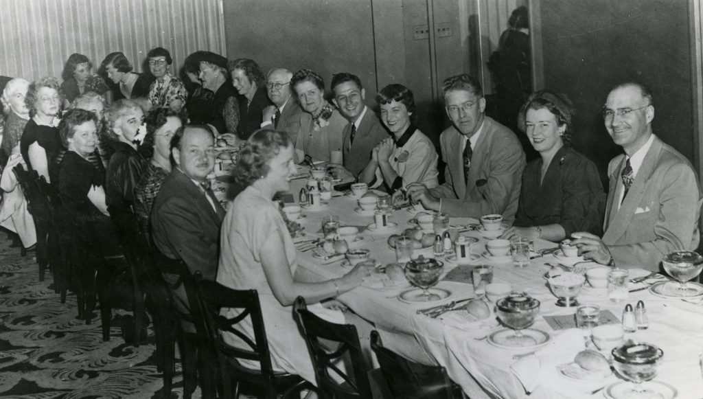 Photo en noir et blanc de personnes assises à une table lors d'un banquet.