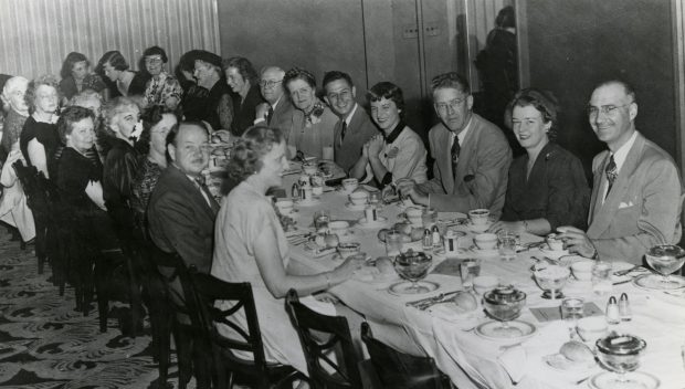 Photo en noir et blanc de personnes assises à une table lors d'un banquet.