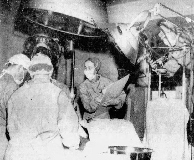 Photo en noir et blanc d'une femme penchée sur une table d'opération, en train de dessiner. À ses côtés, deux médecins. Tous sont vêtus de blouses et de masques.