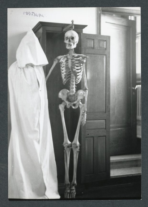 Photo en noir et blanc d'un squelette humain exposé dans une armoire en bois.