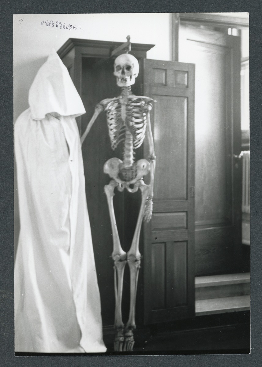 Photo en noir et blanc d'un squelette humain exposé dans une armoire en bois. 
