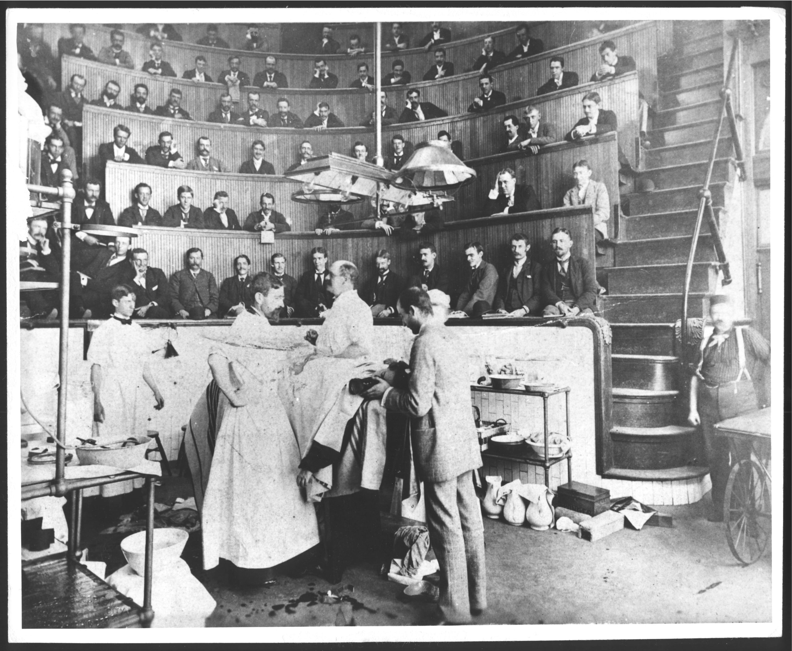 Photo en noir et blanc d'élèves observant une opération dans un amphithéâtre chirurgical à gradins. 
