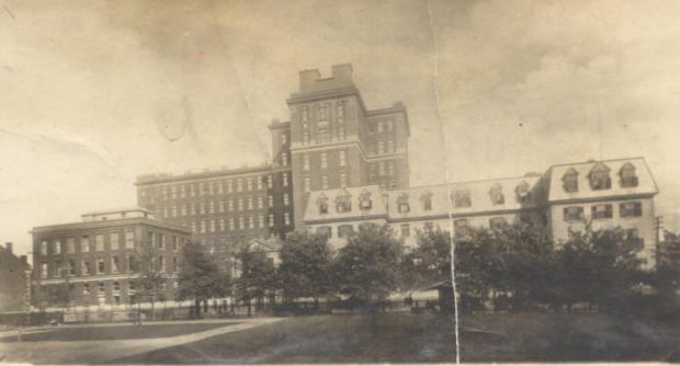 Photographie aux tons sépia présentant un bâtiment d’hôpital du XIXe siècle avec une extension plus contemporaine à l'arrière.