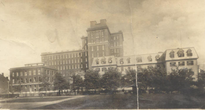 Photographie aux tons sépia présentant un bâtiment d’hôpital du XIXe siècle avec une extension plus contemporaine à l'arrière. 