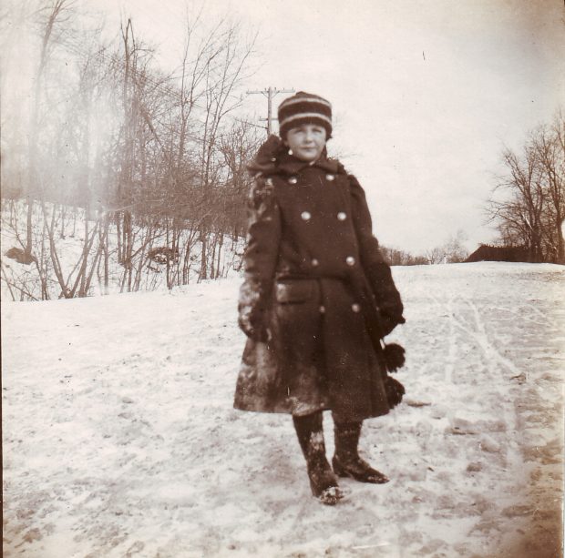 Photographie en noir et blanc d'un enfant en vêtements d'hiver posant sur un chemin enneigé.