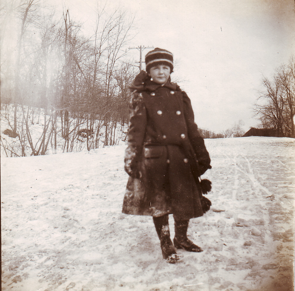 Photographie en noir et blanc d'un enfant en vêtements d'hiver posant sur un chemin enneigé.