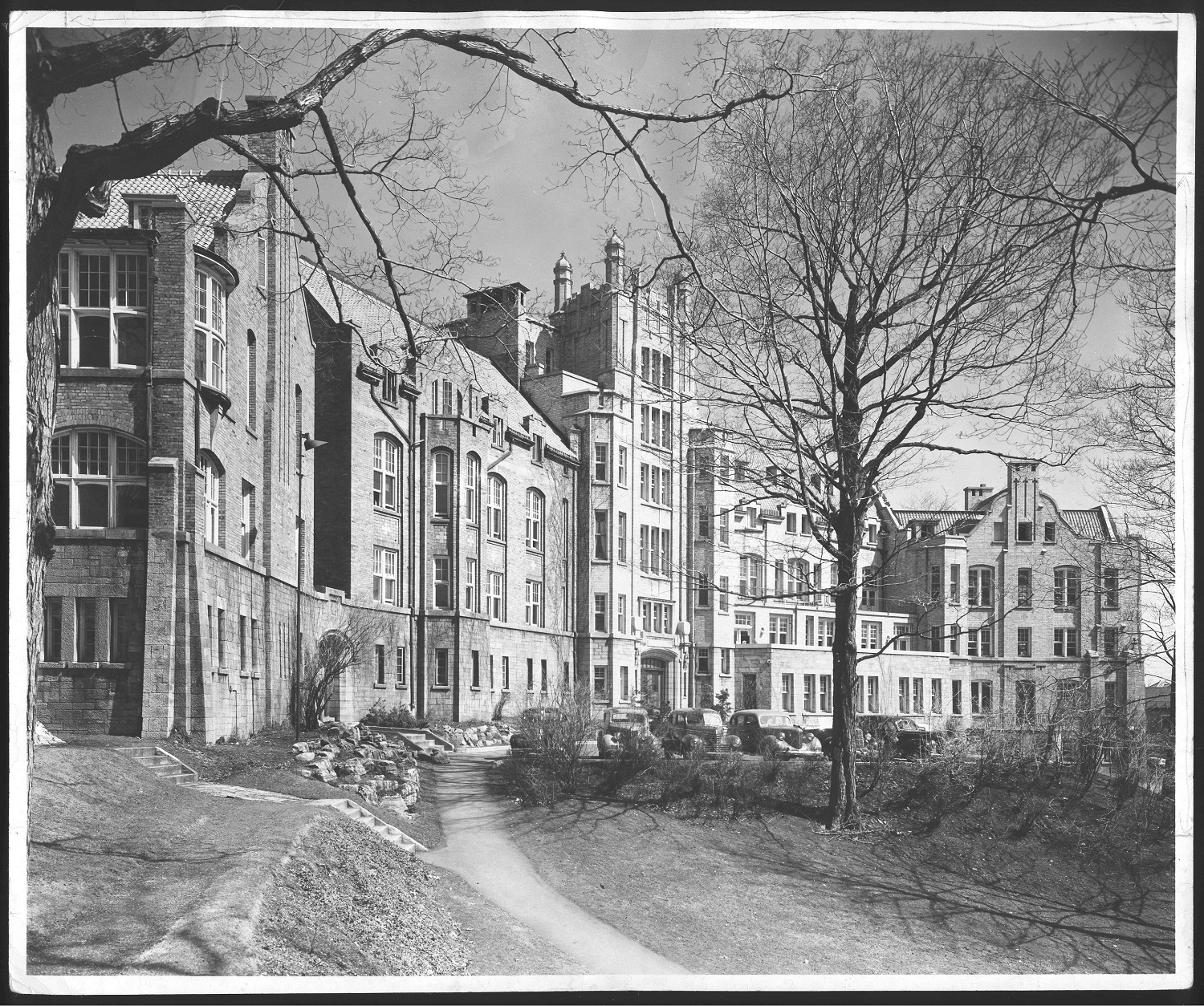 Photo en noir et blanc d'un bâtiment édouardien en briques entouré d'arbres. 