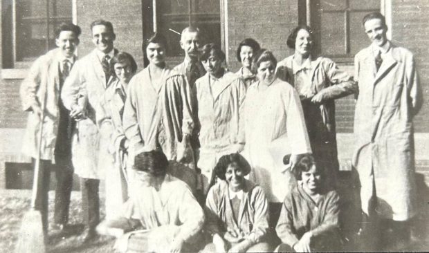 Photo en noir et blanc d'un groupe d'élèves de tous genres, portant des blouses de laboratoire et se tenant en rangs.