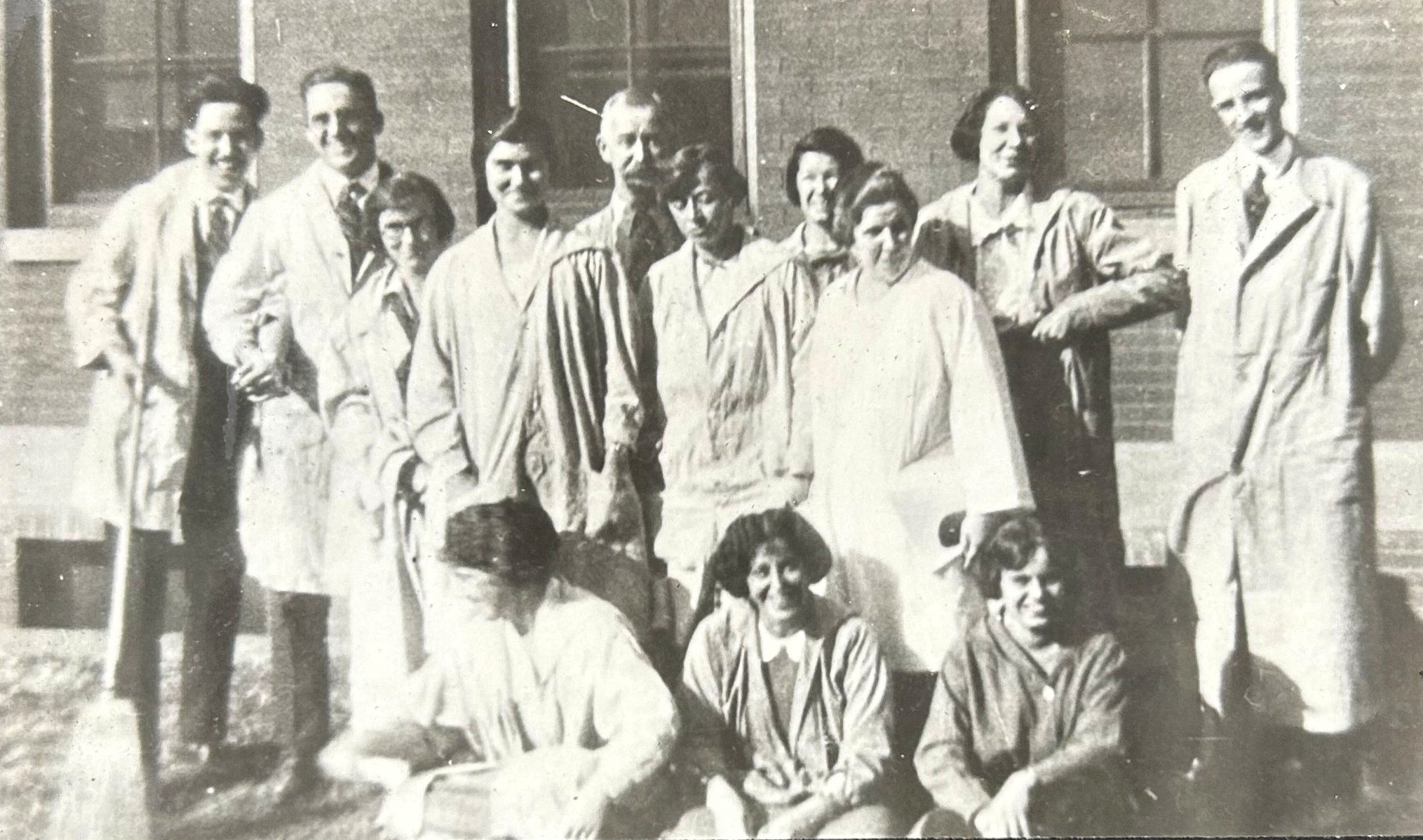 Photo en noir et blanc d'un groupe d'élèves de tous genres, portant des blouses de laboratoire et se tenant en rangs. 