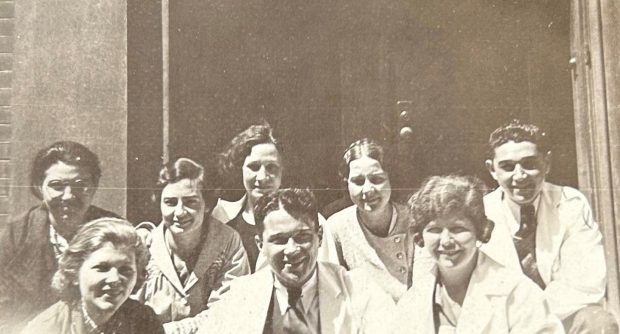 Photo en noir et blanc d'un groupe d'élèves de tous genres portant des blouses de laboratoire et formant deux rangées. La photo est recadrée à hauteur d’épaule.