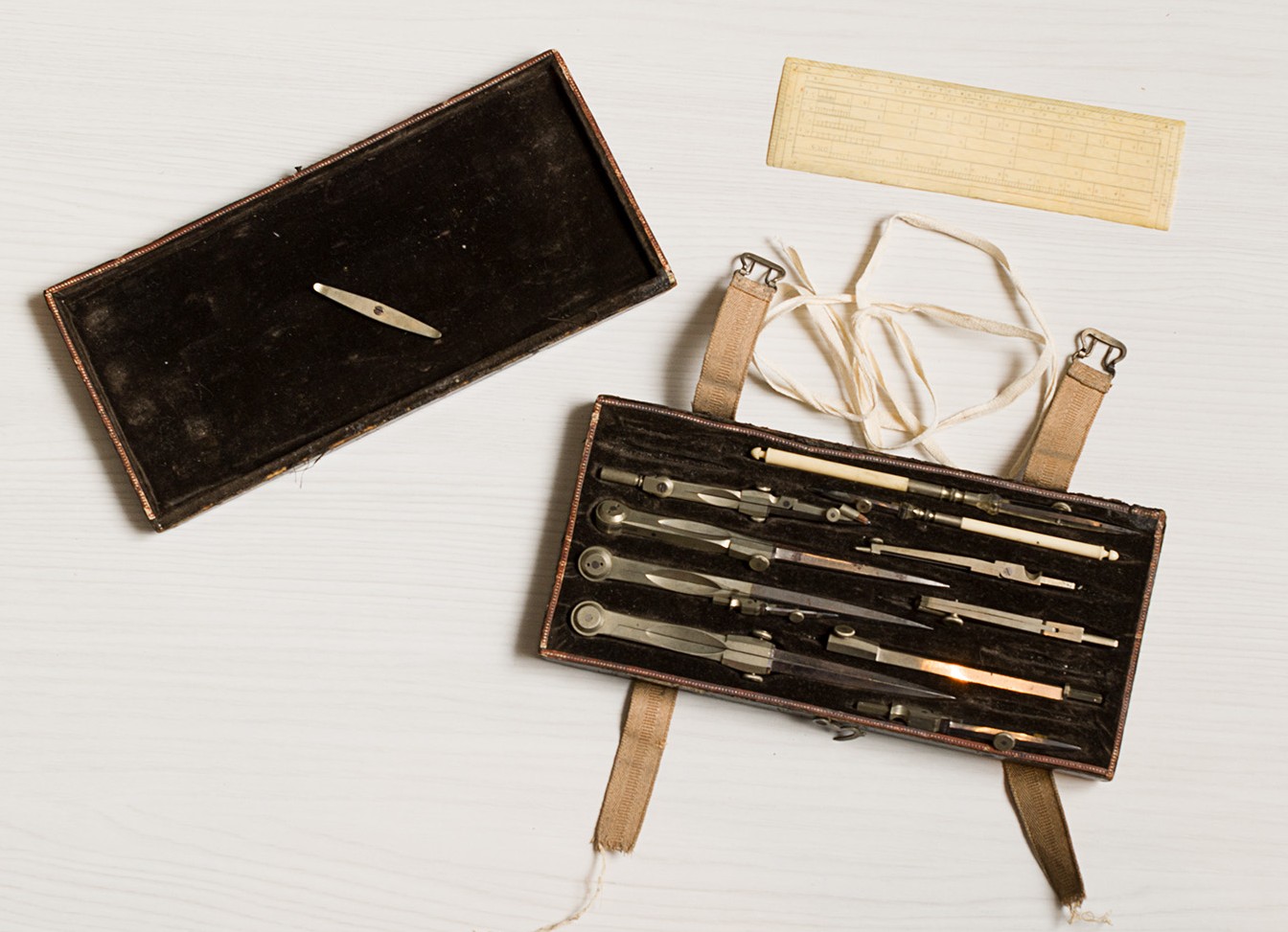 Photo en couleur montrant un coffret entrouvert avec un intérieur feutré foncé contenant de petits outils en métal et en os. 