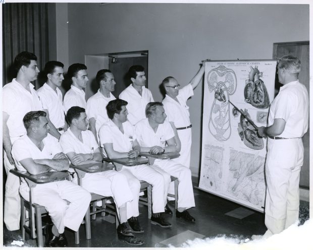 Photo en noir et blanc d'un homme enseignant à des aides-soignants à partir d'une illustration médicale.
