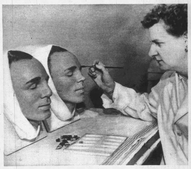 Image en noir et blanc d’un artiste médical utilisant un pinceau pour peindre des sourcils sur deux moulages médicaux de têtes masculines.