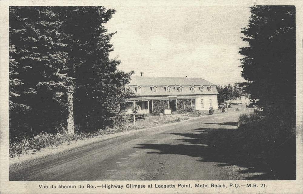 Carte postale présentant une photographie noir et blanc de l’hôtel Killiecrankie. Au premier plan, un chemin en terre bordée d’une forêt d’épinette. Entre les épinettes sur le côté gauche du chemin apparaît l’hôtel le Killiecrankie. L’hôtel est un long bâtiment de 2 étages construit en bois. La façade présente une véranda envahie par une vigne.