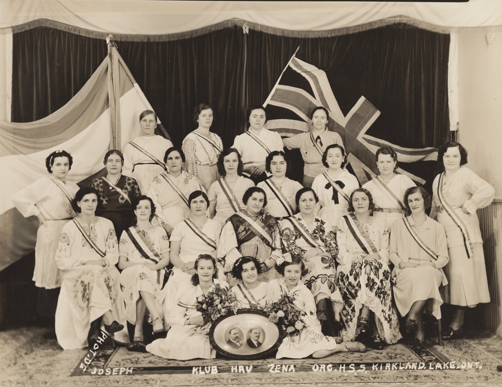 Portrait photographique de quatre rangées de filles et de femmes portant des robes et des écharpes de couleur claire, devant deux drapeaux – le drapeau croate et l’Union Jack.