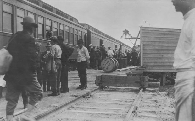 Photographie en noir et blanc d’un train de voyageurs à la gare de Swastika. Des personnes montent ou descendent du train.