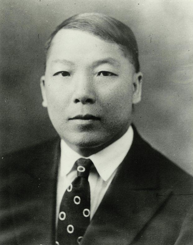 Portrait photographique en noir et blanc de Charlie Chow en jeune homme portant un costume et une cravate.