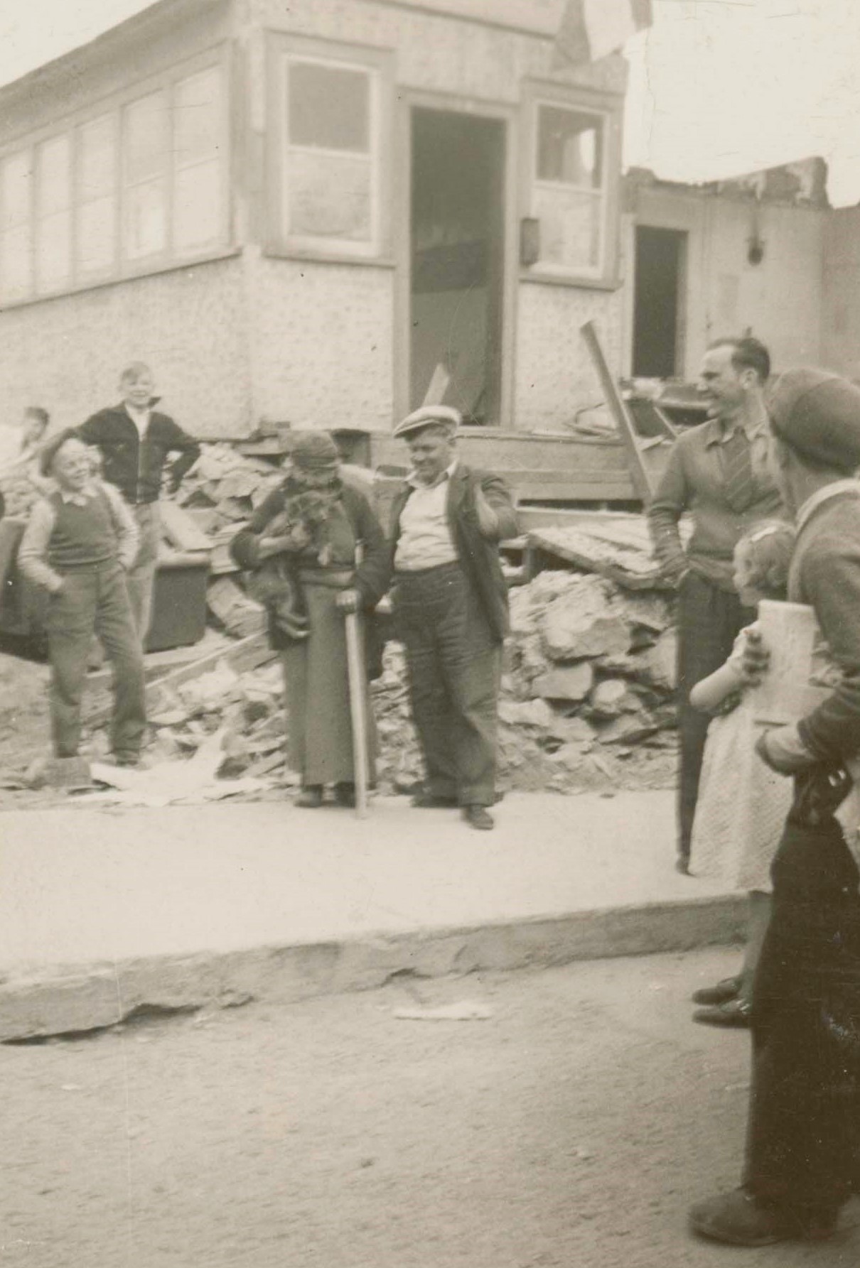 Photographie en noir et blanc prise à l’extérieur d’un bâtiment en cours de démolition. Une petite foule se tient devant.