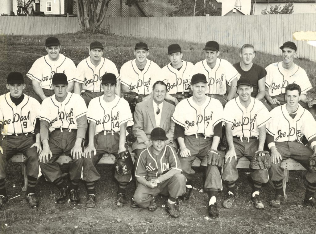 Photographie en noir et blanc de joueurs de baseball et d’un préposé aux bâtons, la plupart sont en uniforme. Le parrainage de Joe Dash est inscrit sur chaque maillot de l’équipe.