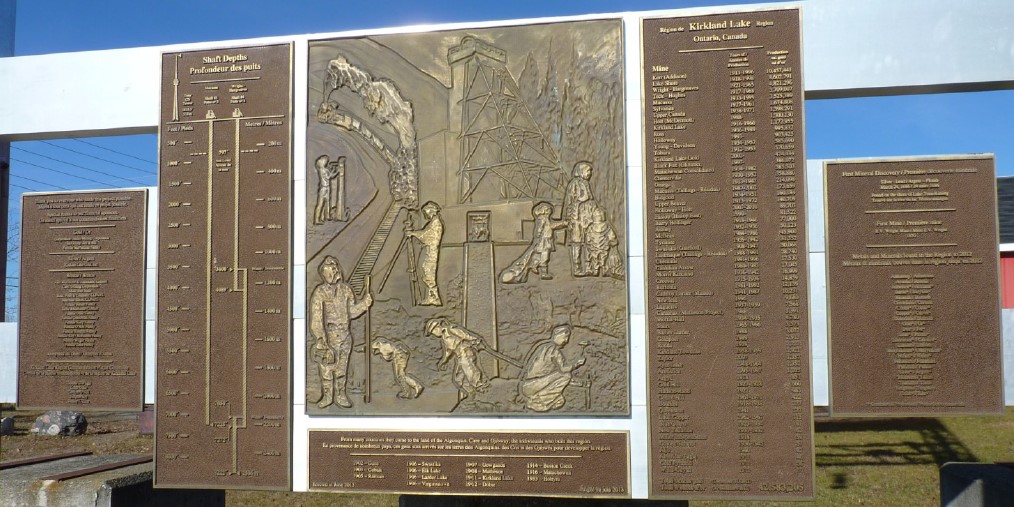 Photographie couleur d’une grande plaque de bronze située sur le site de la mine Toburn à Kirkland Lake. L’image centrale représente l’histoire de la communauté.