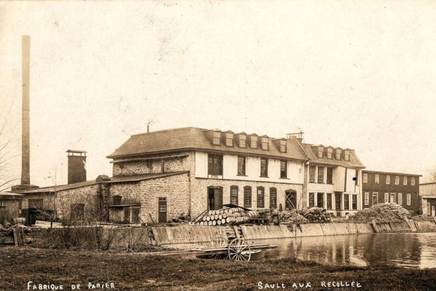 Carte postale publiée vers 1900. Au centre : la fabrique de papier avec, à sa gauche, sa haute cheminée sur la digue des moulins encombrée de tonneaux et de matériaux.  À l'avant-plan: un quai roulant donne sur le bassin d’eau.