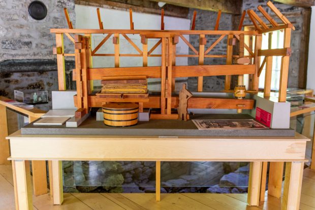 Posée sur une table dans la maison du Pressoir, cette maquette en bois représente la presse à pommes construite par Didier Joubert et son intégration à la charpente du bâtiment à l’époque. La presse est un grand levier abaissé progressivement par une vis sans fin, actionnée par la force humaine.