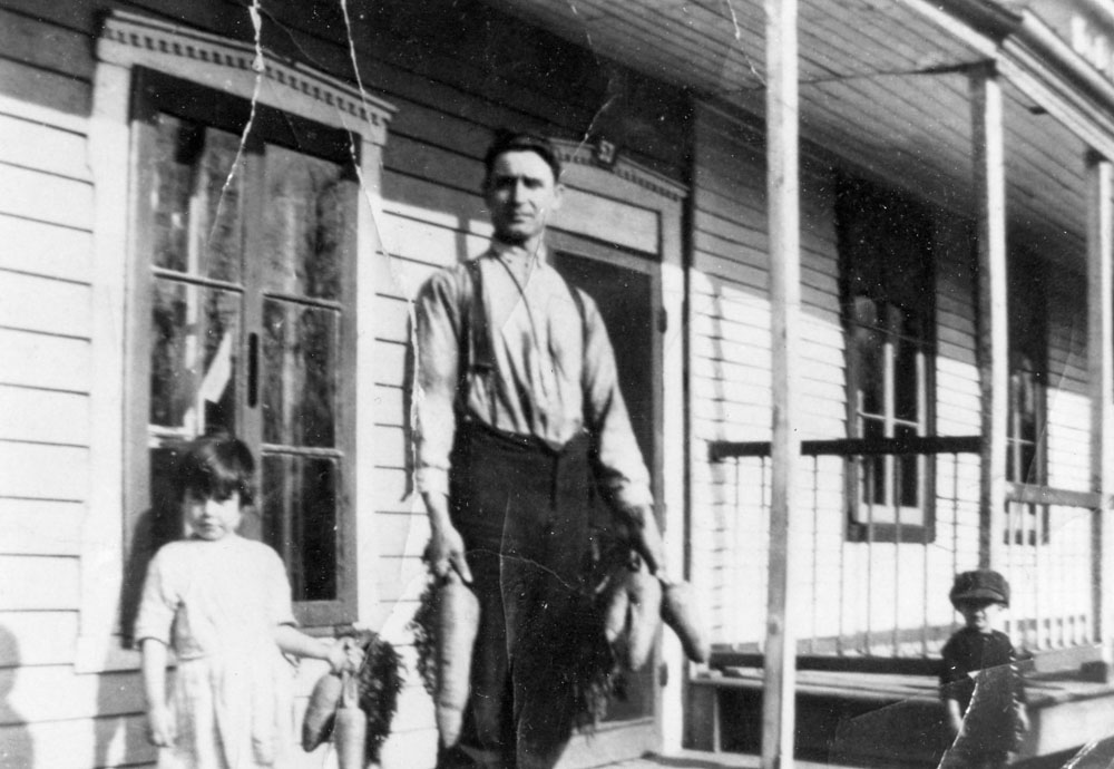 Alphonse Mérineau, au centre, et sa fille Georgette, à gauche, devant leur logement de la rue du Pressoir. Ils tiennent des grosses carottes dans leurs mains. Le petit fils Alfred Mérineau est à droite, près de la galerie, avec une casquette sur la tête.
