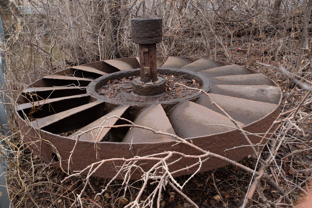 Une roue à pales rouillée qui provient d’une turbine hydraulique a été déposée au sol près de la maison du Meunier.