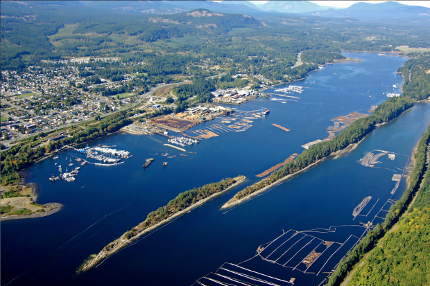 Photo aérienne oblique en couleur d'une ville située sur le rivage d'un plan d'eau étroit et allongé, avec des îles boisées et bordée de collines couvertes de forêts.