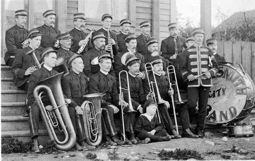 Photo en noir et blanc de vingt membres d'un ensemble musical en uniforme tenant leurs cuivres et leurs instruments à vent.