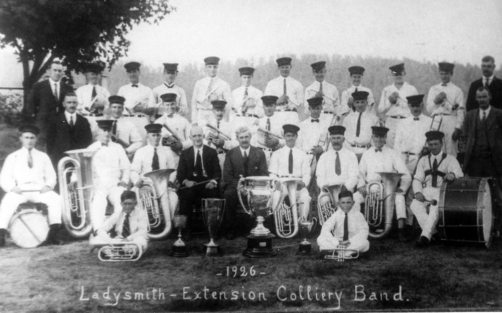 Une trentaine de musiciens en uniforme posent en trois rangs avec leurs instruments derrière quatre trophées en argent.
