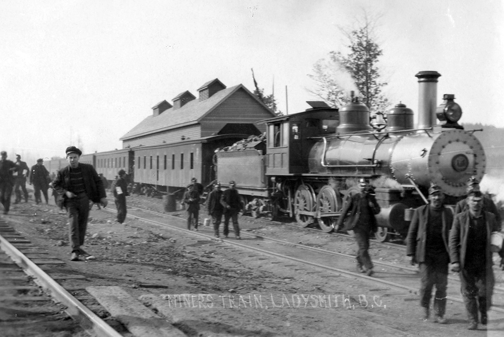 Photo en noir et blanc représentant des hommes sortant d'un train dirigé par une locomotive à vapeur.