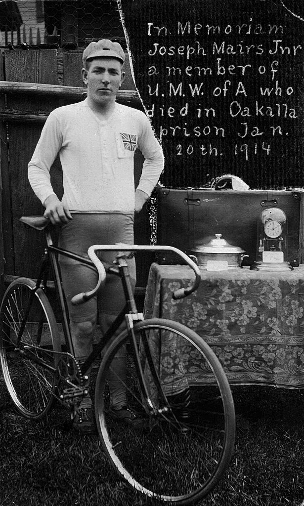 Photo en noir et blanc montrant un jeune homme à côté d'une bicyclette de course du début des années 1900.