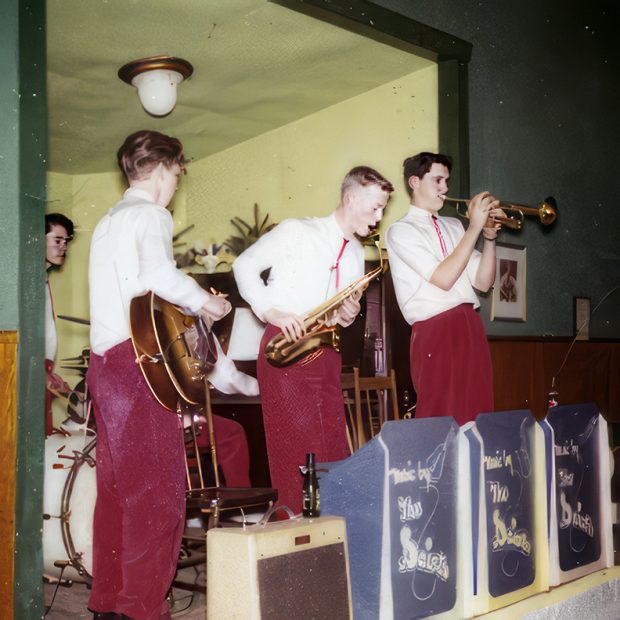 Photo en couleur de cinq jeunes musiciens rasés de près, portant des chemises blanches à manches longues, des cravates bolo et des pantalons rouges, debout sur scène, jouant de la trompette, du saxophone, de la guitare acoustique, de la batterie et du piano.