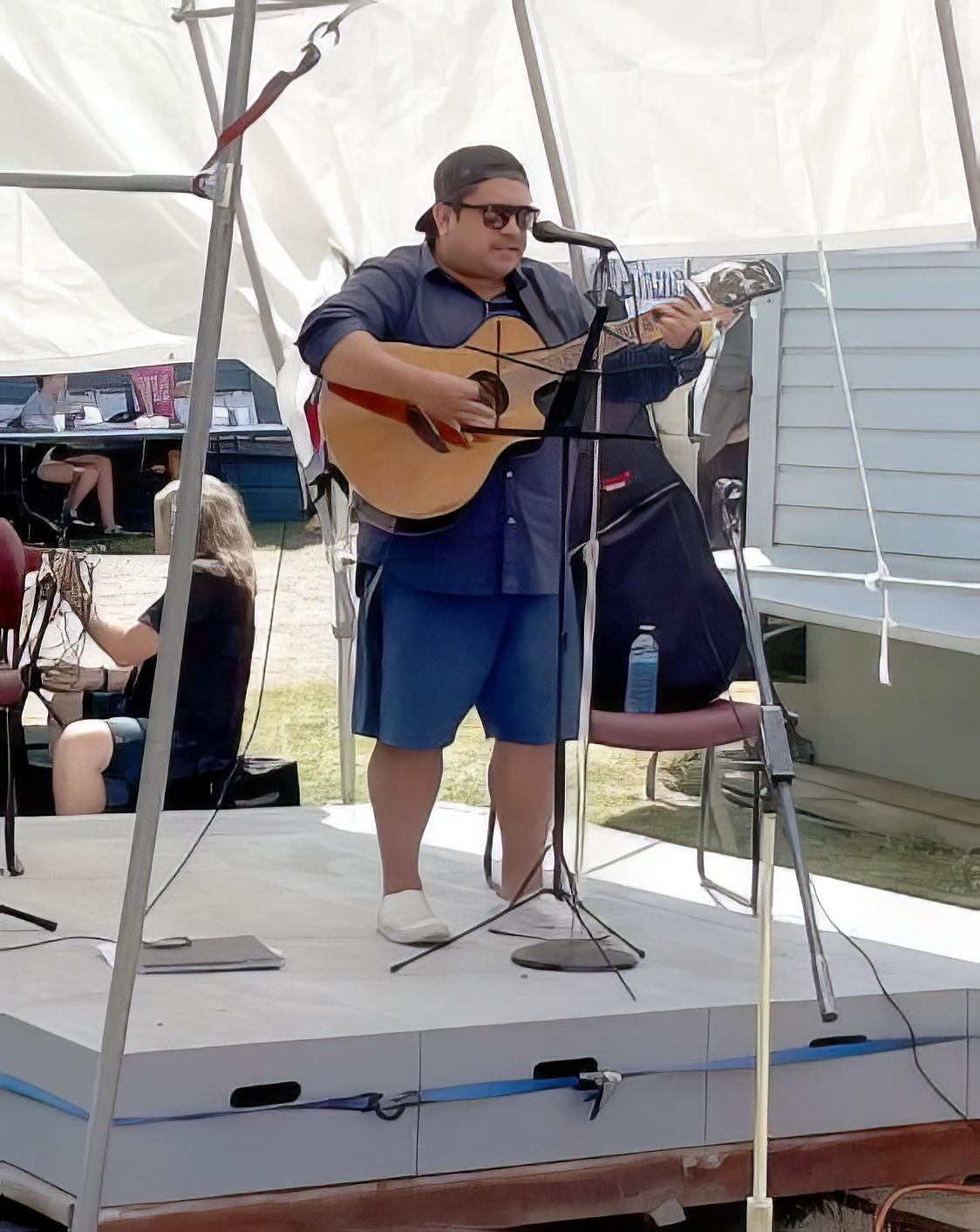 Photo en couleur d'un musicien Salish de la côte sur scène, devant un microphone, jouant de la guitare acoustique électrifiée et chantant.
