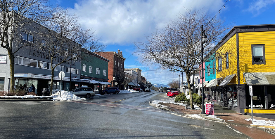 Photo en couleur d'une rue commerciale bordée de bâtiments patrimoniaux, certains avec des façades en bois peintes de couleurs vives, d'autres en stuc gris et d'autres encore en brique rouge