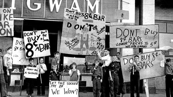 Photo en noir et blanc d'un groupe d'enfants se tenant devant un magasin nommé WigWam, certains léchant des cornets de crème glacée, tenant des pancartes portant des variantes de la phrase « Ne soyez pas dupes, n'achetez pas de barres à 8 cents ».