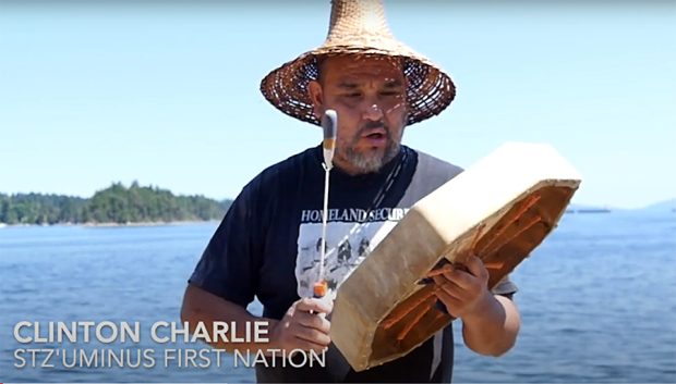 Photo couleur d'un homme Salish de la côte portant un chapeau traditionnel en cèdre et jouant du tambour cérémoniel.