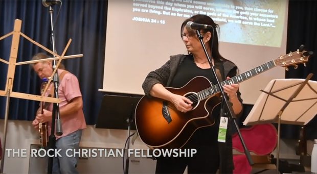 Photo couleur de deux artistes jouant de la guitare sur scène. Diaporama avec des passages bibliques.