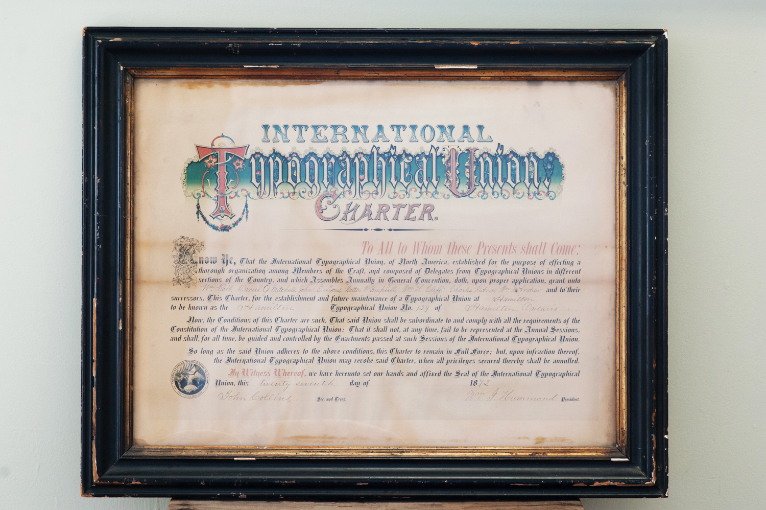 Photographie de la charte de l’International Typographical Union (syndicat international du secteur typographique) datant de 1872. La charte signée en papier utilise une calligraphie classique et est enserrée dans un cadre en verre et en bois.
