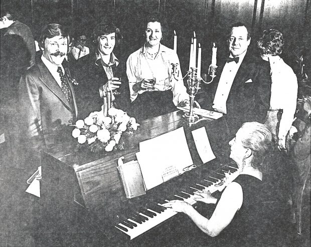 Quatre membres du conseil d'administration s’interposent près d’un piano durant une soirée 