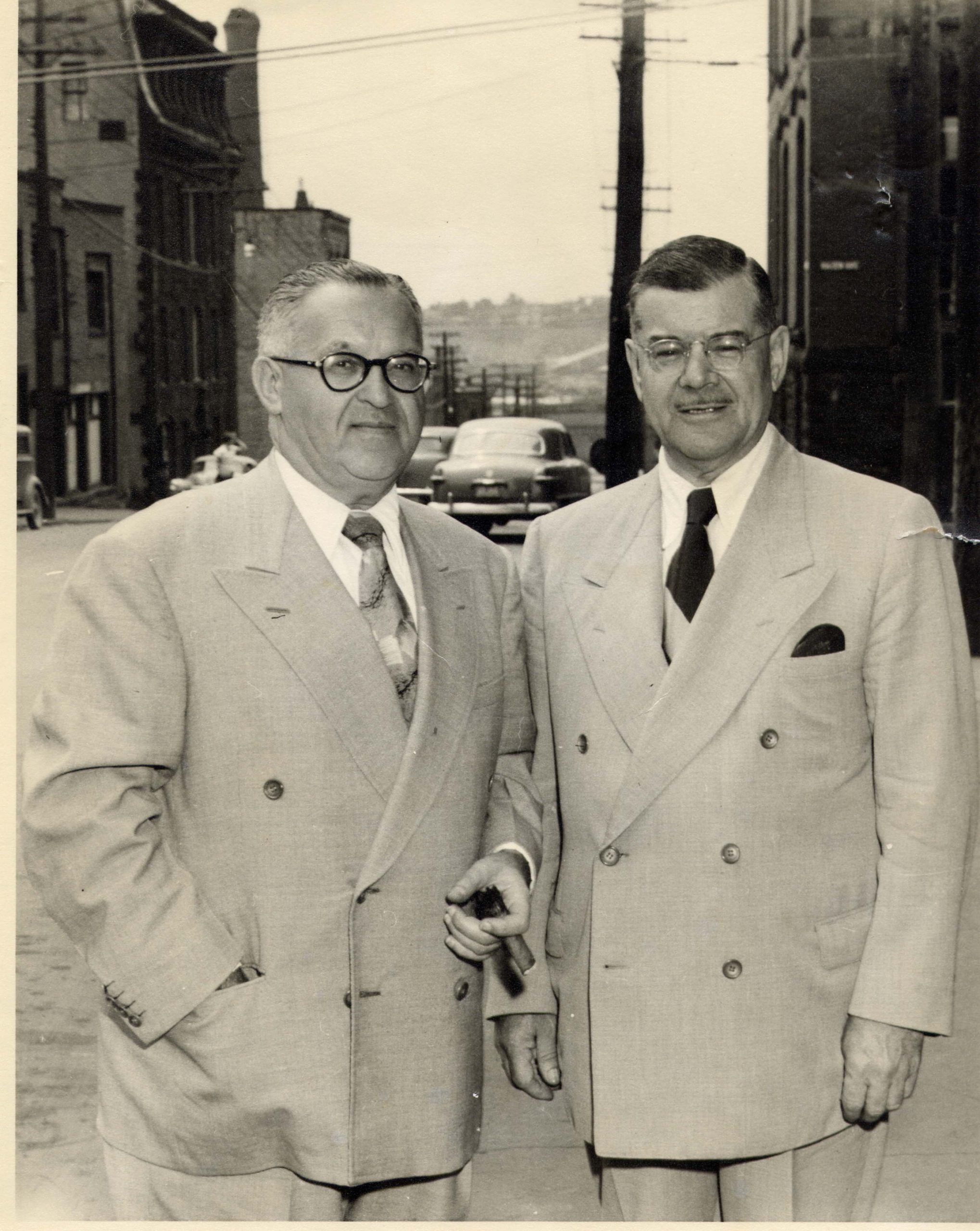 Deux hommes d’affaires en costume à double boutonnage se tiennent sur le trottoir.