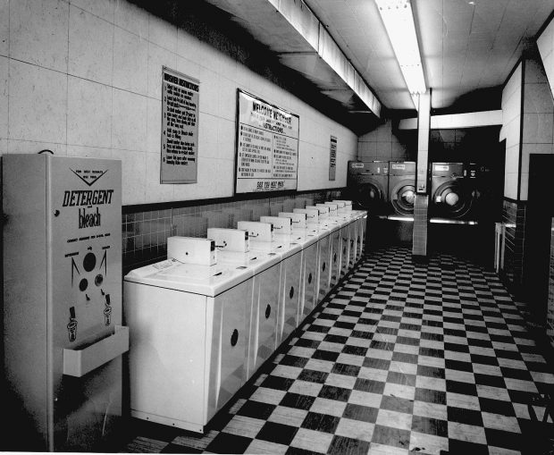 Rangée de dix machines à laver avec un distributeur de lessive. De grandes sécheuses sont installées sur le mur arrière.