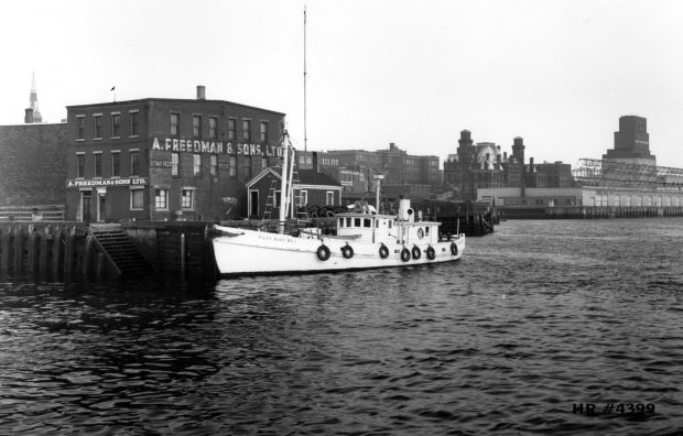 Bateau-pilote amarré au quai devant l’entrepôt à trois étages de la société A. Freedman and Sons, Ltd.